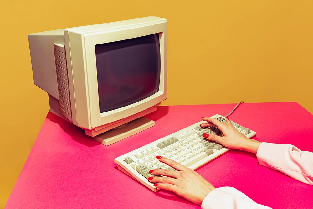 WebP image of person typing on old keyboard and tube monitor with red nails