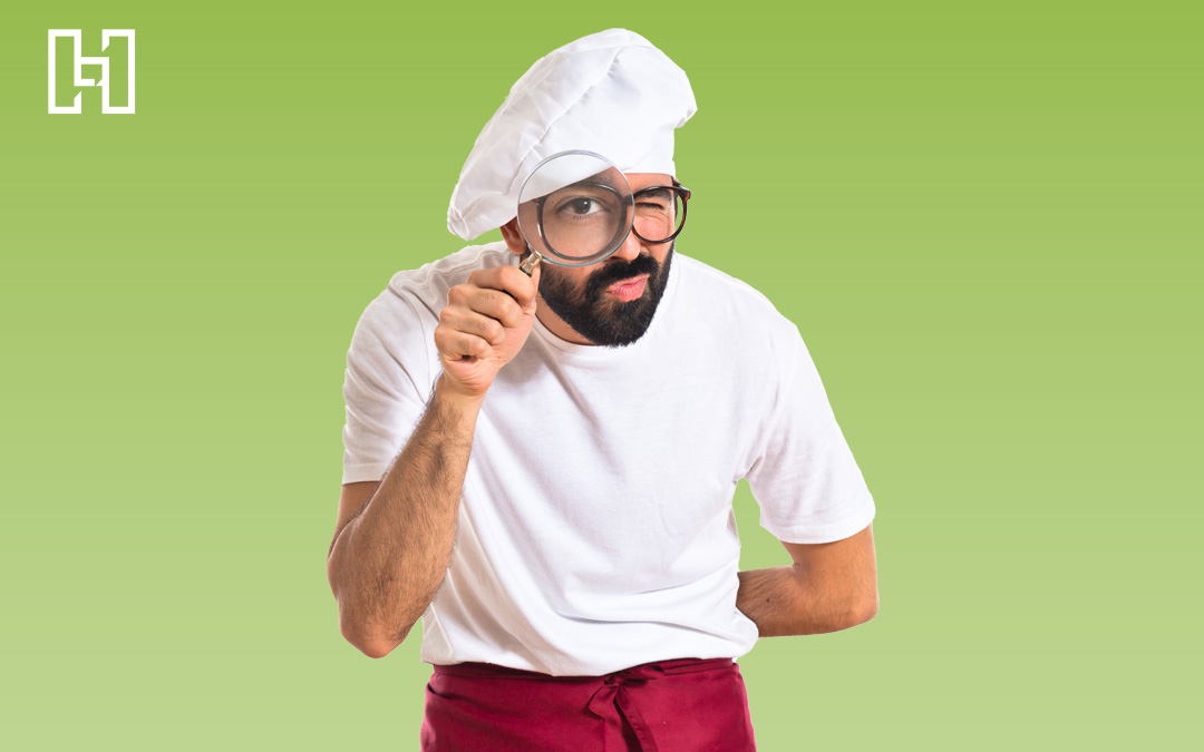 Chef with a white hat and apron looking through magnifying glass