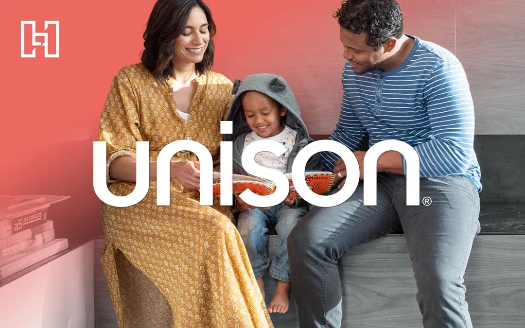 Woman, man, and child sitting together reading a picture book with Hurrdat and Unison logos in front